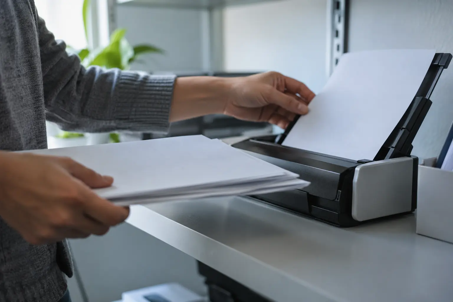 A hand feeds documents into a desktop scanner.
